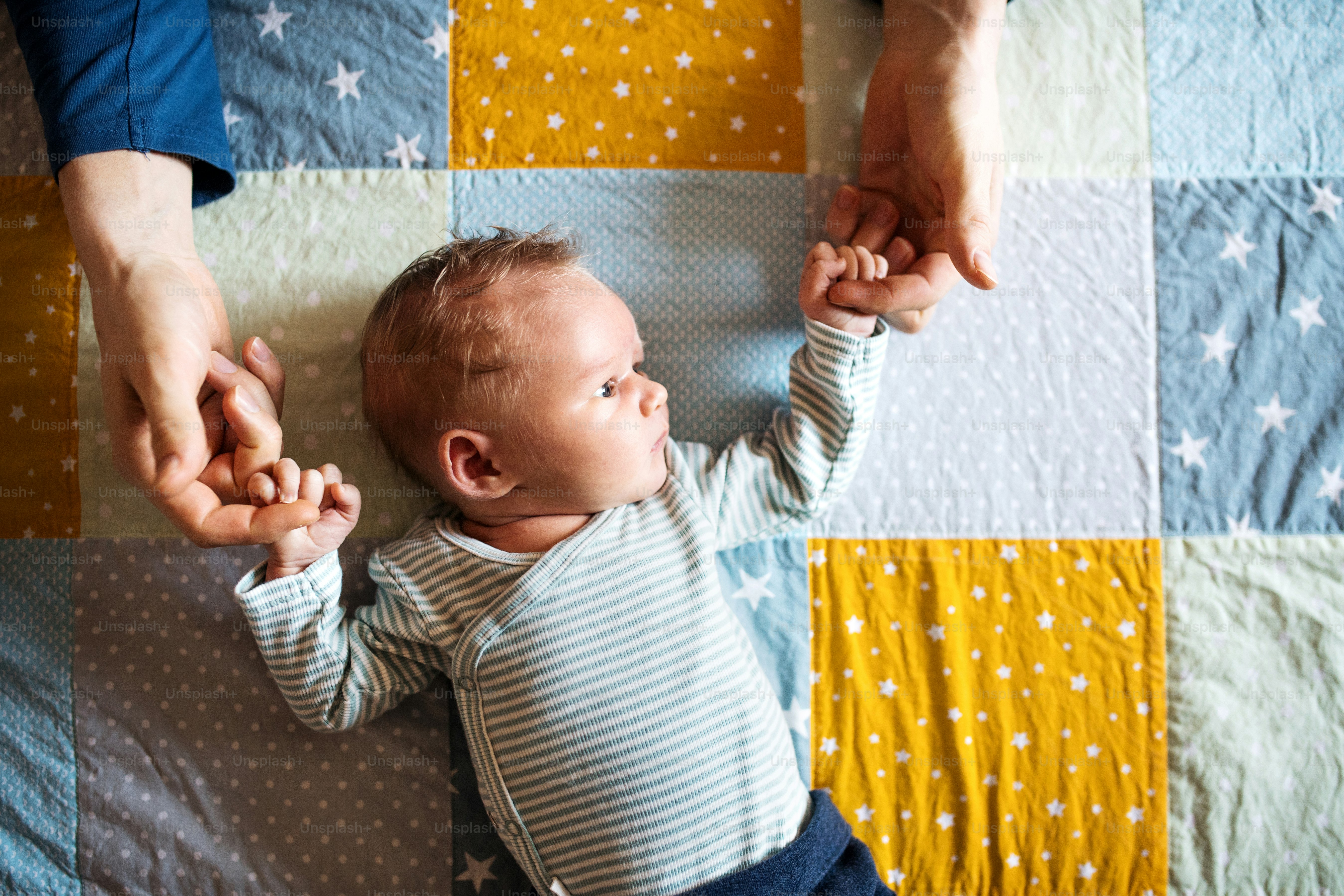 A top view of a newborn baby lying on bed on a quilted blanket at home.