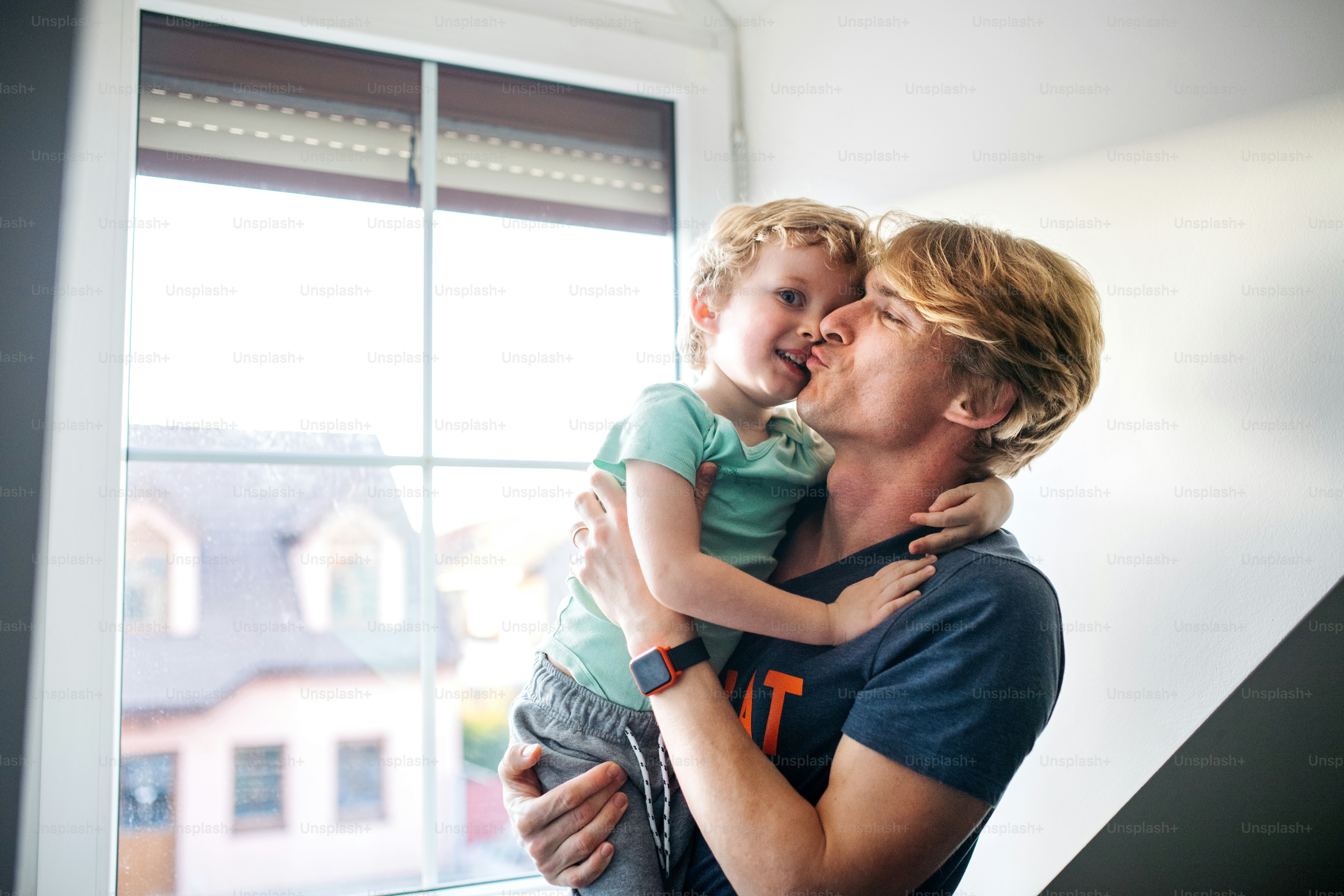A happy father holding a toddler son at home, kissing.
