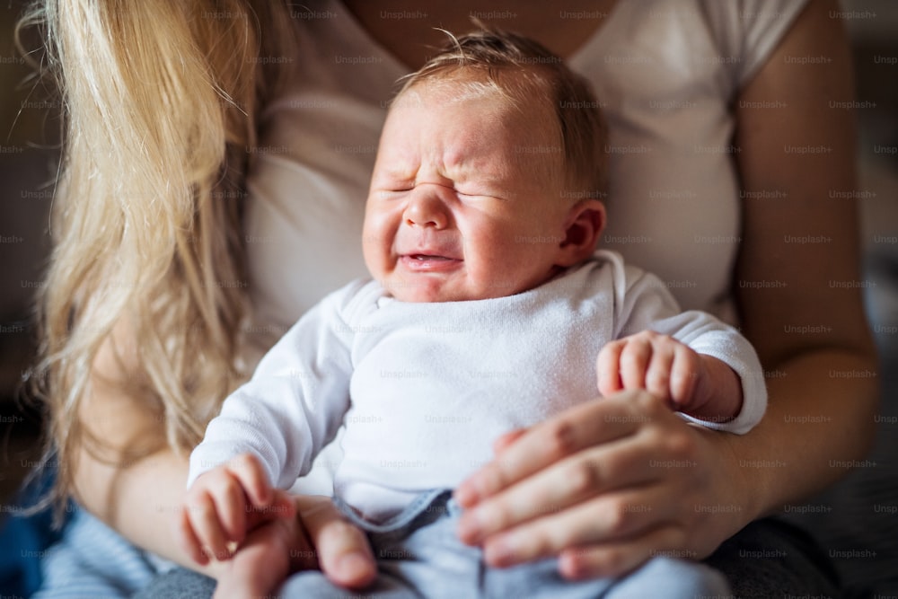 Una sección media de madre irreconocible sosteniendo a un bebé recién nacido llorando en casa.