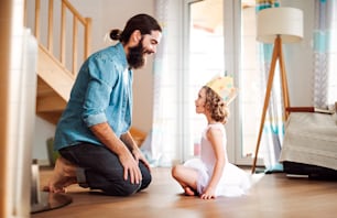 A side view of small girl with a princess crown and young father at home, playing.