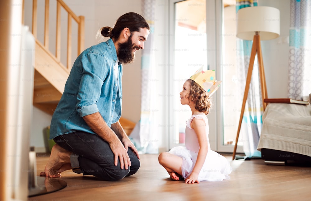 Eine Seitenansicht eines kleinen Mädchens mit einer Prinzessinnenkrone und einem jungen Vater zu Hause, der spielt.