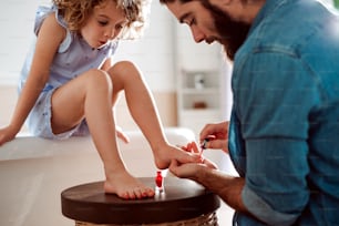 A young father painting small daughter's nails in a bathroom at home.