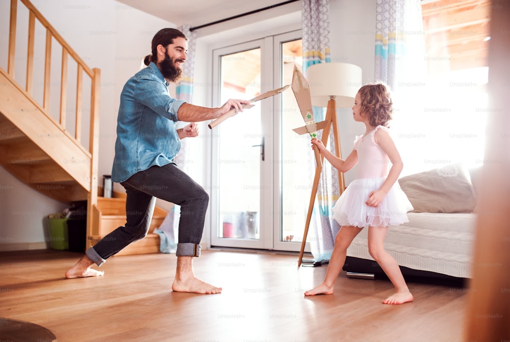 A small girl and young father with paper swords at home, fighting and playing.