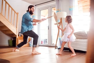 Uma menina pequena e um jovem pai com espadas de papel em casa, lutando e brincando.