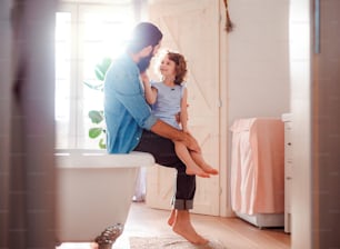 A happy small girl with young father in bathroom at home, talking.