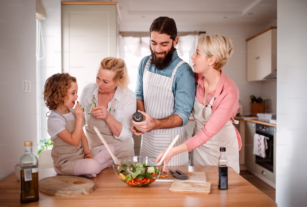A portrait of small girl with parents and grandmother at home, preparing vegetable salad.