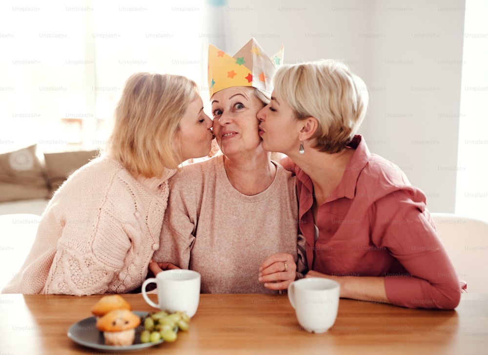 A happy senior mother with two adult daughters sitting at the table at home, having fun.