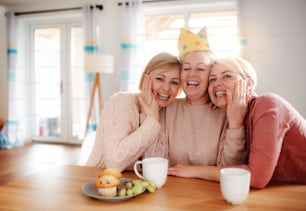 Una madre anziana felice con due figlie adulte sedute al tavolo di casa, divertendosi.