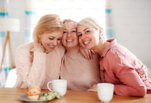 Una madre anziana felice con due figlie adulte sedute al tavolo di casa.