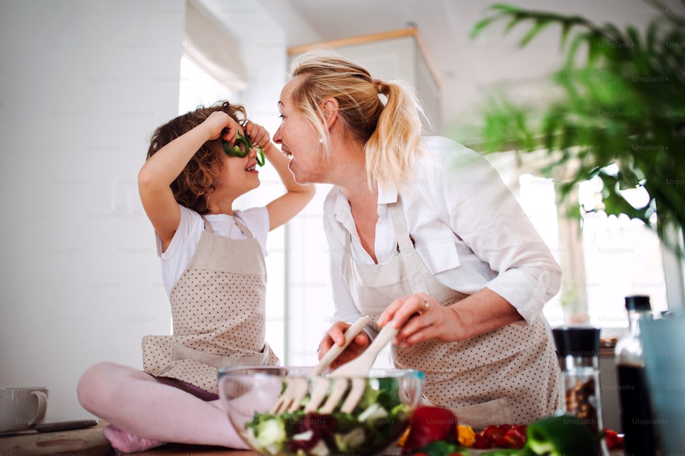 Un portrait de petite fille heureuse avec grand-mère préparant une salade de légumes à la maison, s’amusant.