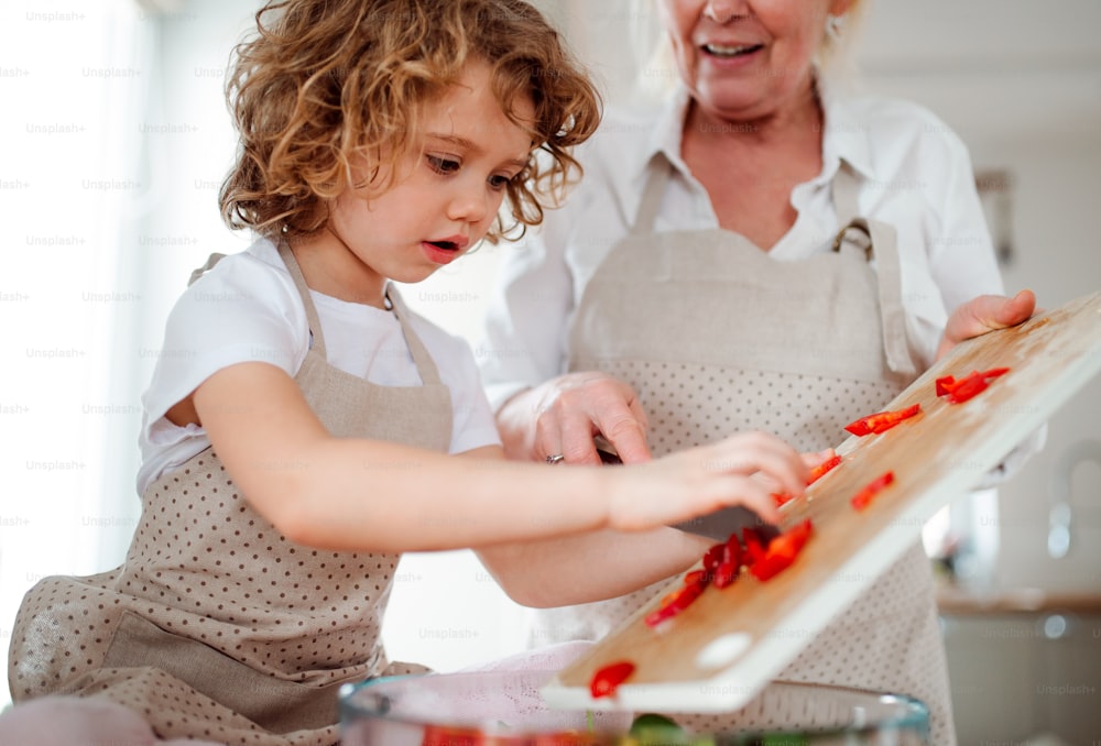 Un ritratto di bambina con la nonna in una cucina a casa, preparando insalata di verdure.