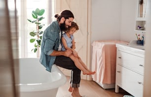A small girl with young father in bathroom at home, looking at painted nails on feet.