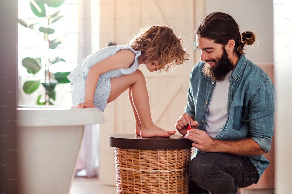A young father painting small daugter's nails in a bathroom at home.
