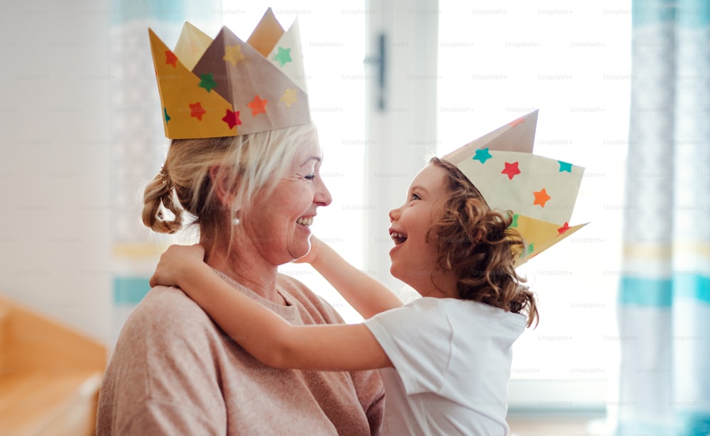 A portrait of small girl and grandmother with paper crown having fun at home.