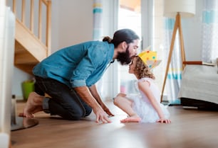 Una vista laterale di una bambina con una corona di principessa e un giovane padre a casa, che si bacia quando gioca.