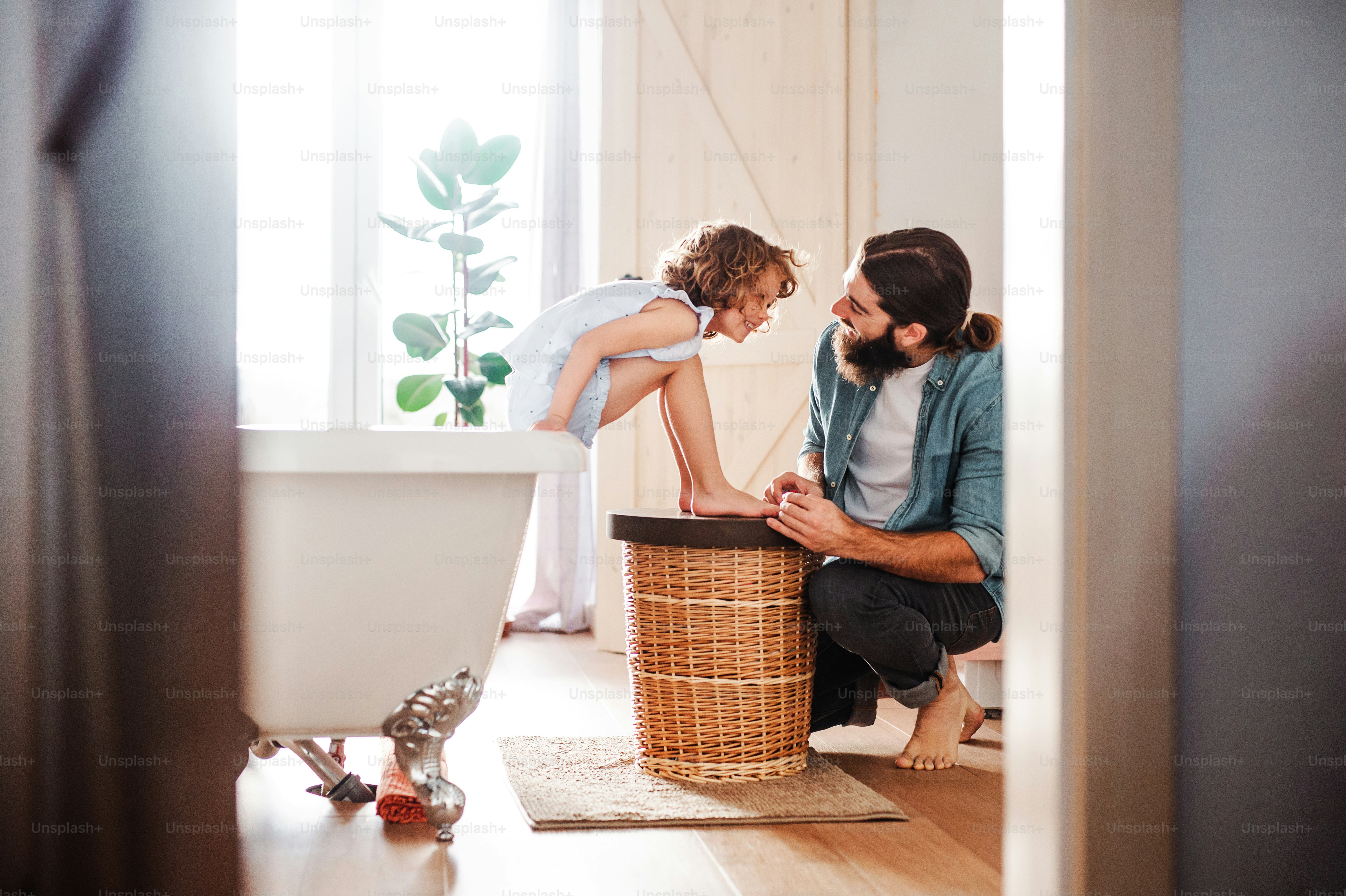 A young father painting small daugter's nails in a bathroom at home.