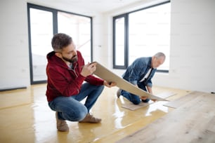 A rear and top view of mature man with his senior father laying vinyl flooring, a new home concept.