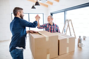 A portrait of mature man with his senior father shaking hands when furnishing new house, a new home concept. Copy space.