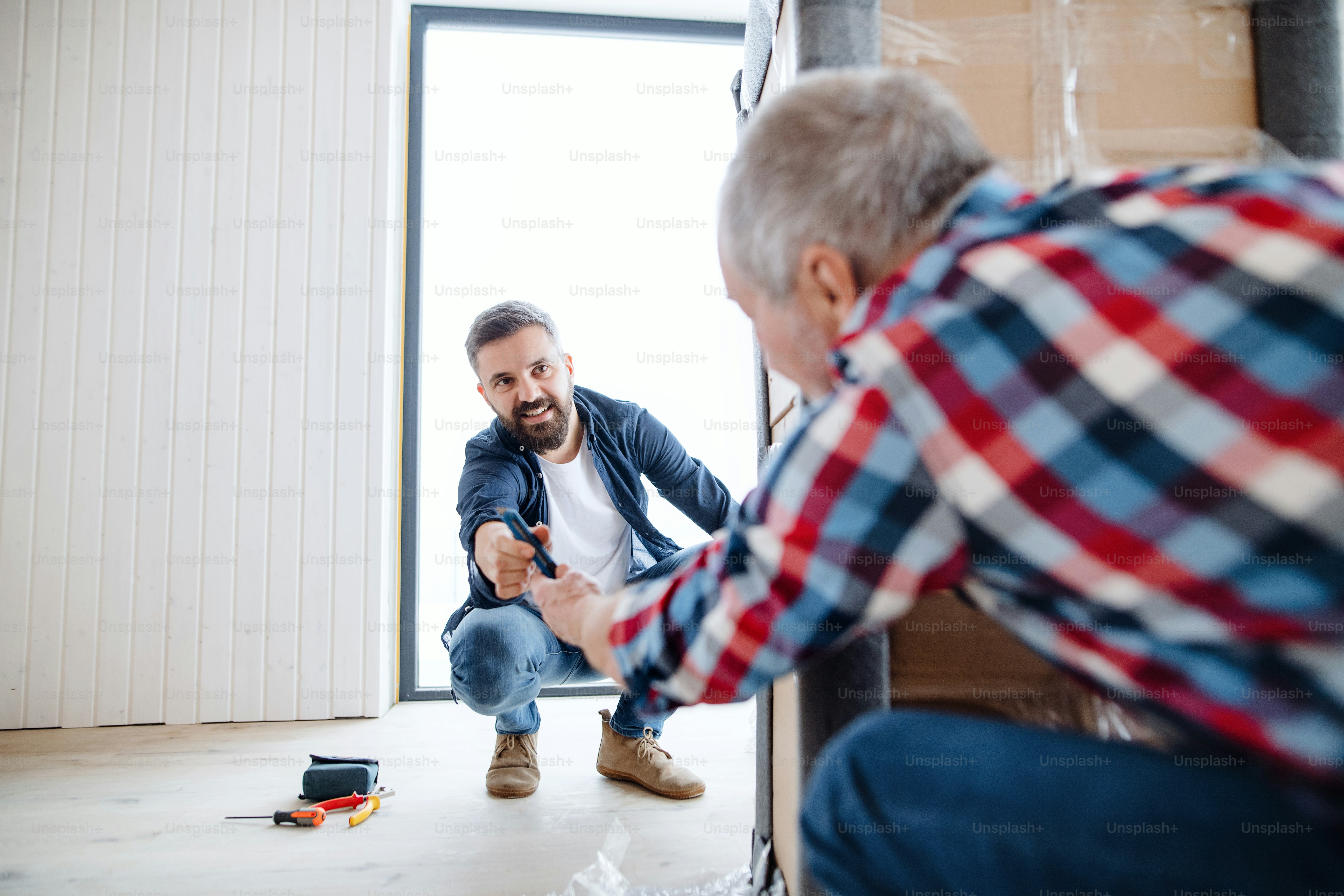 Ein fröhlicher älterer Mann, der seinem reifen Sohn bei der Einrichtung eines neuen Hauses, eines neuen Wohnkonzepts hilft.