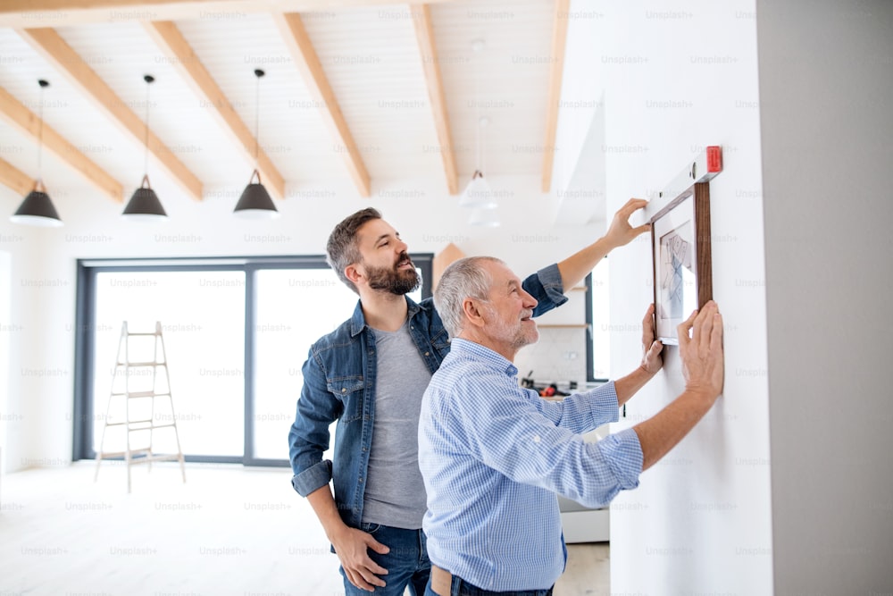 A senior man helping his son hanging up pictures on a wall, a new home concept.