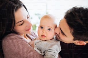 Um retrato em close-up de um jovem casal feliz com um bebê dentro de casa.