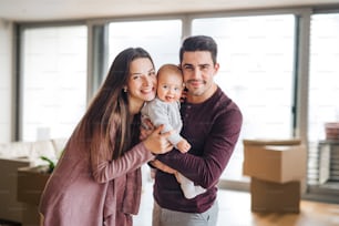 Un retrato de una joven pareja feliz con un bebé y cajas de cartón, mudándose a un nuevo hogar.