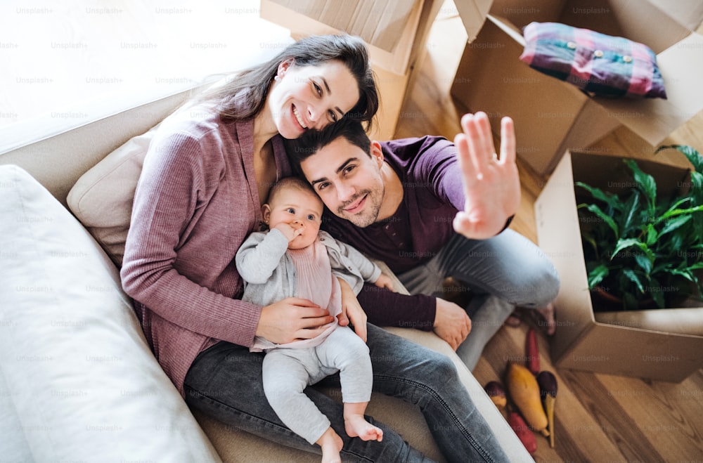 A portrait of happy young couple with a baby and cardboard boxes, moving in a new home. A top view.