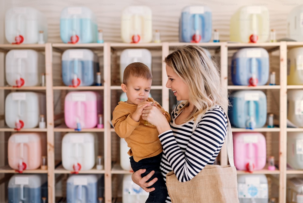 Una giovane donna attraente con un bambino che compra liquidi in un negozio a rifiuti zero.