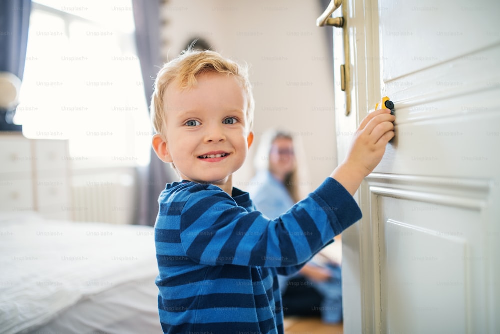 A happy toddler boy standing by the door inside in a bedroom, playing with car.