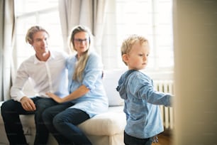 Happy young happy parents looking at their toddler son inside in a bedroom.