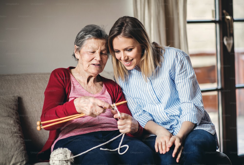 Una abuela anciana enseñando y una nieta adulta para tejer en casa.