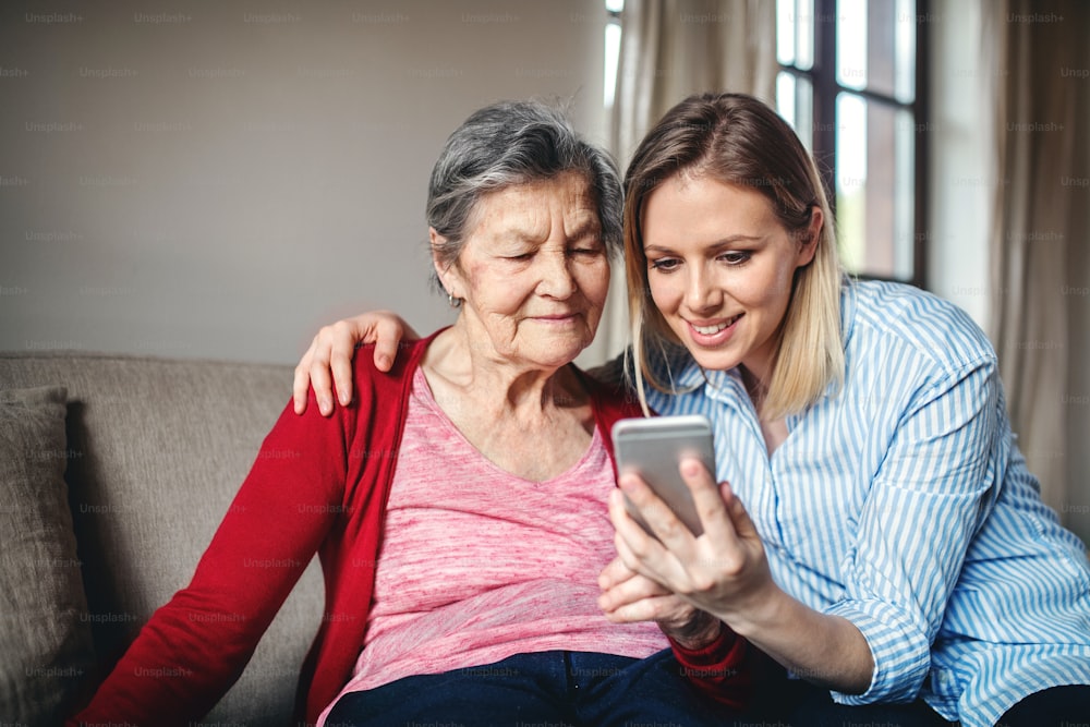 Eine ältere Großmutter und eine erwachsene Enkelin mit Smartphone zu Hause.