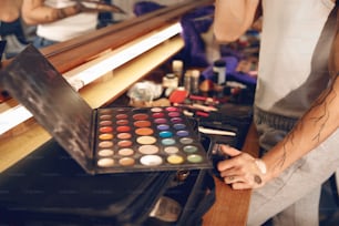 Una persona sosteniendo una paleta de maquillaje frente a un espejo
