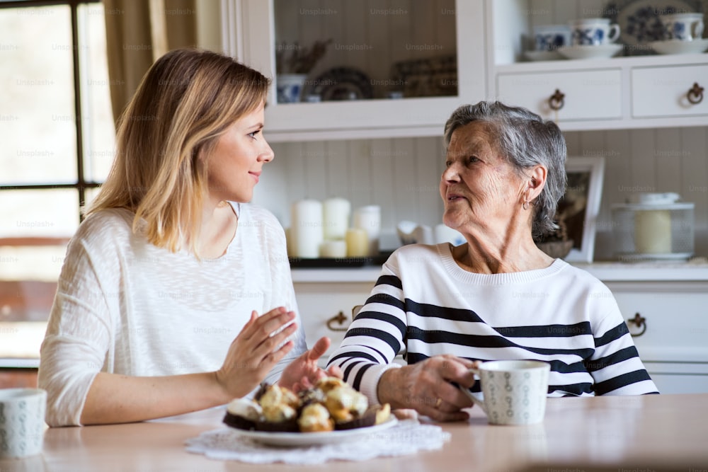 Portrait of an elderly grandmother with an adult granddaughter at home. Women sitting at the table, eating cakes and drinking coffee.