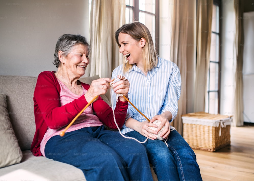 An elderly grandmother and adult granddaughter at home, having fun knitting.