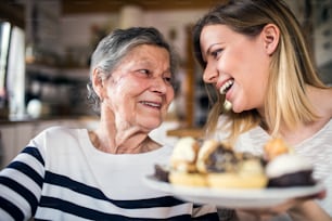 Portrait of an elderly grandmother with an adult granddaughter at home. Women sitting at the table, holding a plate full of cakes.