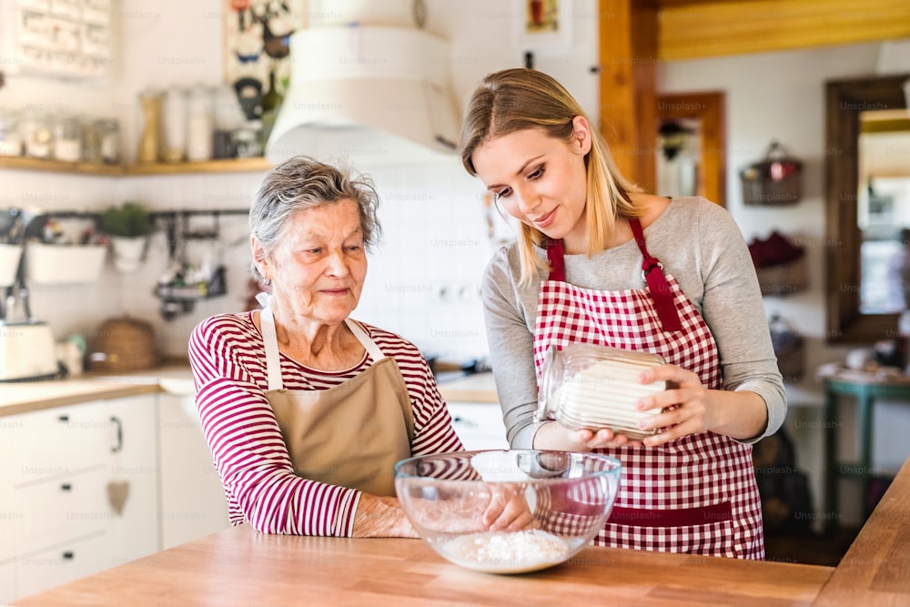 A happy elderly grandmother with an adult granddaughter at home, baking.