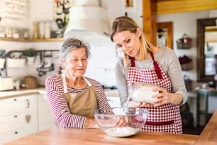 A happy elderly grandmother with an adult granddaughter at home, baking.