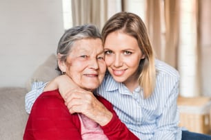 Retrato de uma avó idosa com uma neta adulta sentada no sofá em casa.