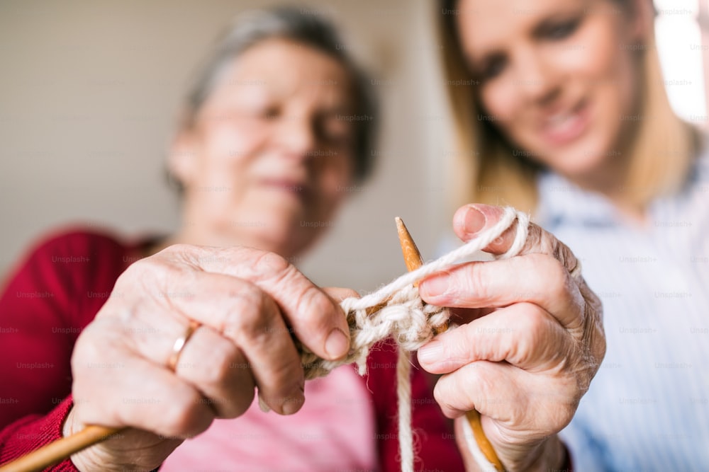 An elderly grandmother and adult granddaughter at home, knitting.