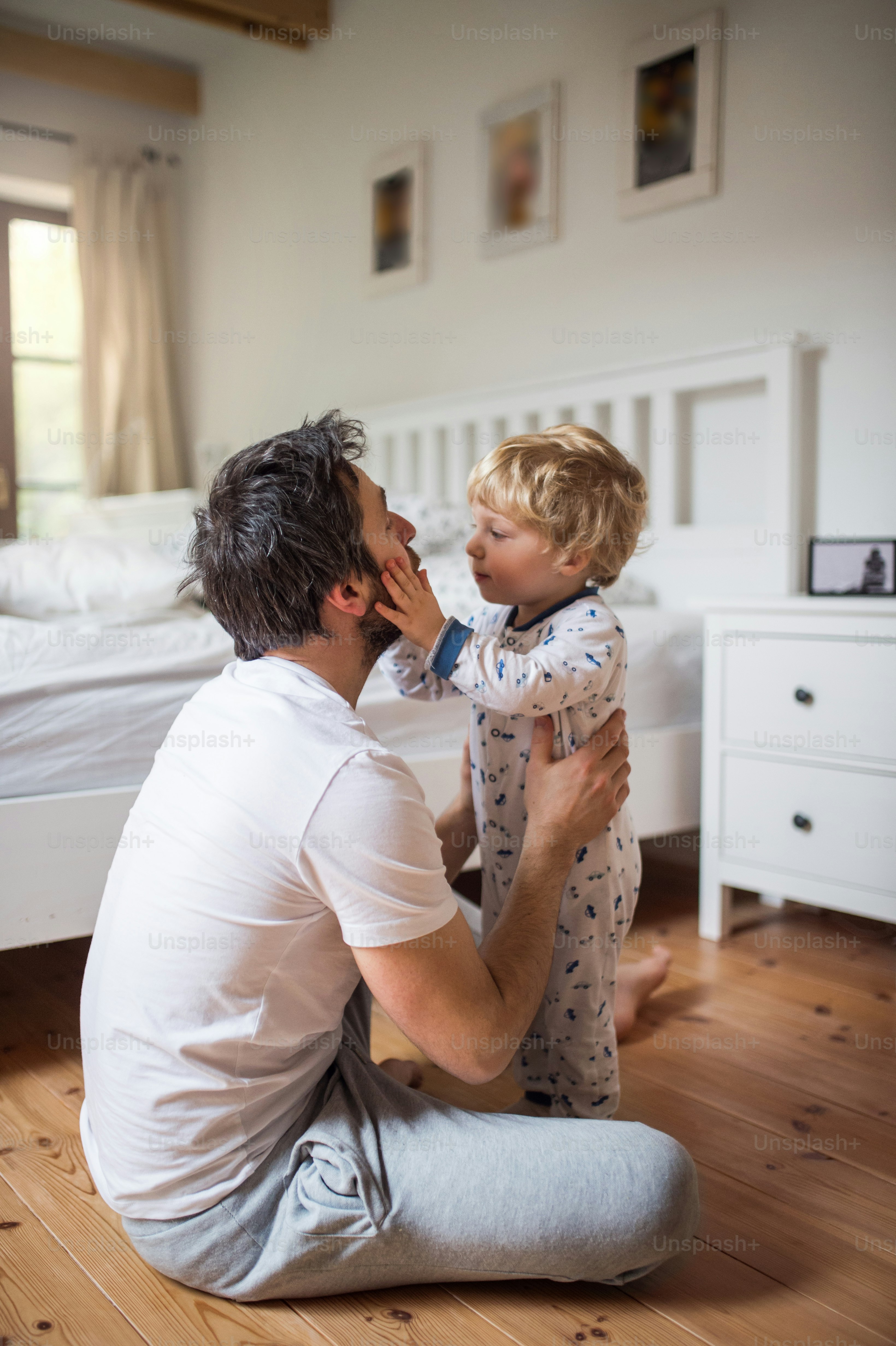 Alter Vater mit einem kleinen Jungen, der vor dem Schlafengehen auf dem Boden im Schlafzimmer zu Hause sitzt. Vaterschaftsurlaub.