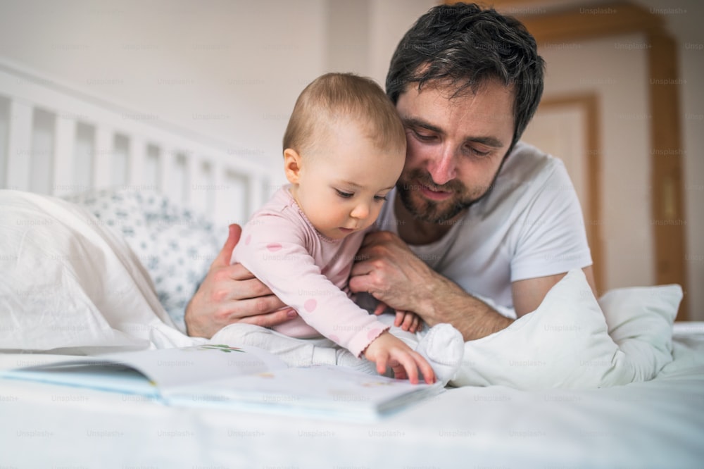 Padre maduro con una niña pequeña en el dormitorio en casa, leyendo cuentos a la hora de acostarse. Paternidad.