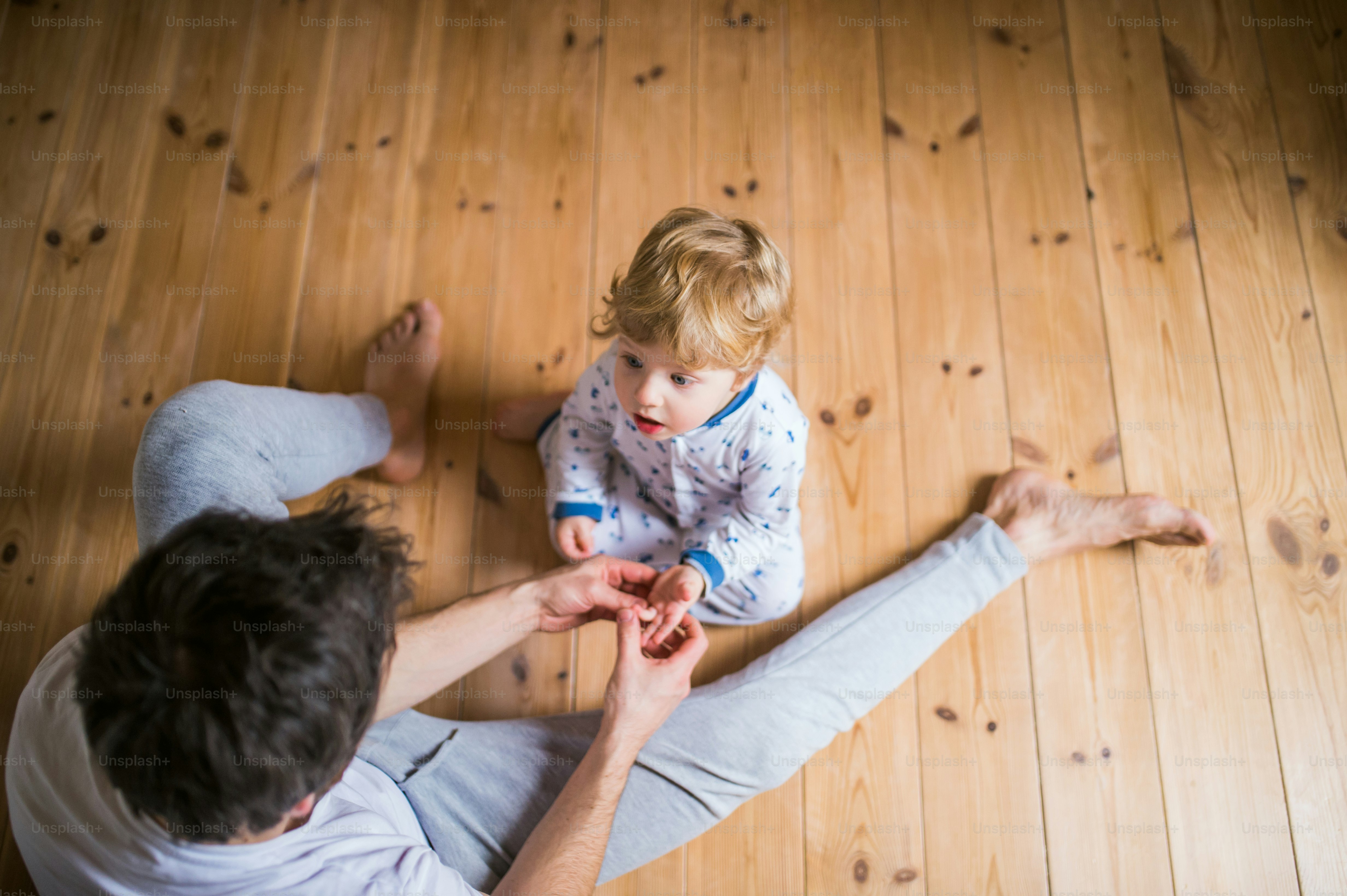 Unkenntlicher Vater mit einem kleinen Jungen, der vor dem Schlafengehen auf dem Boden im Schlafzimmer zu Hause sitzt. Vaterschaftsurlaub. Draufsicht.
