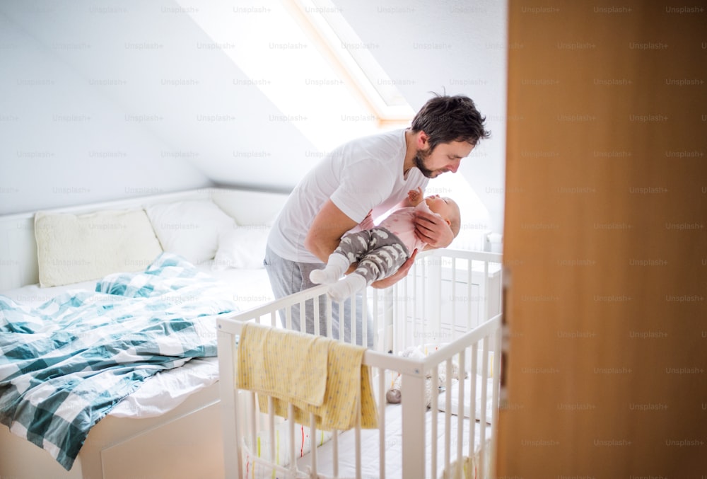 성숙한 아버지는 잠자는 어린 소녀를 집에 있는 유아용 침대에 눕힌다. 육아휴직.
