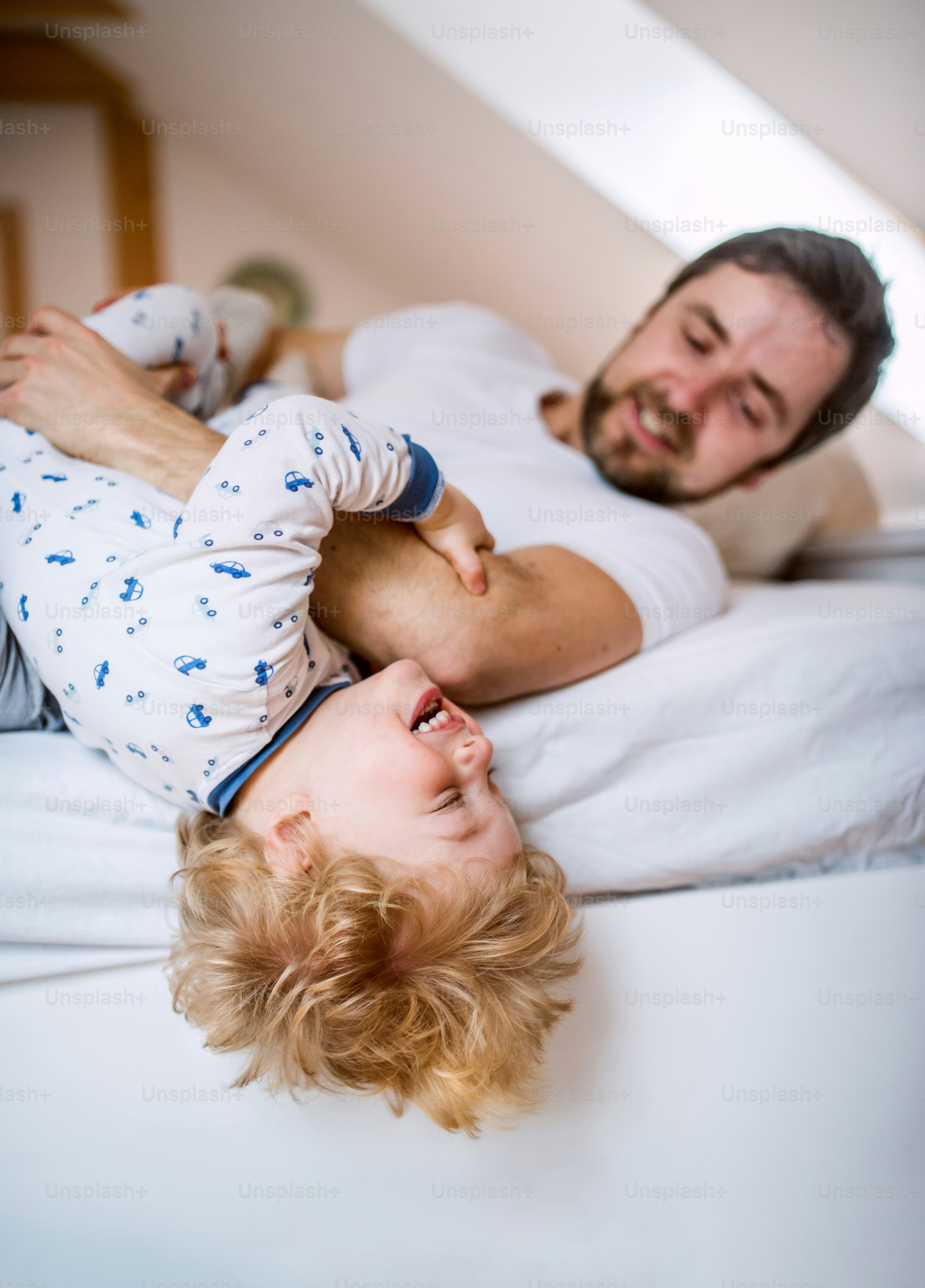Reifer Vater mit einem kleinen Jungen, der sich vor dem Schlafengehen im Schlafzimmer zu Hause amüsiert. Vaterschaftsurlaub.