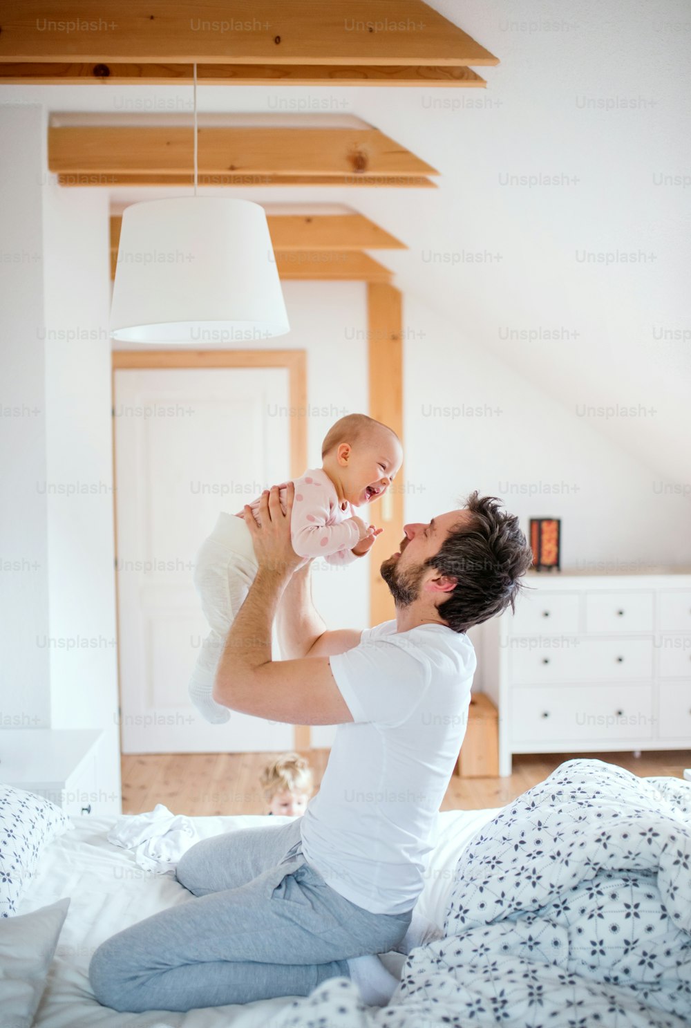 Padre che tiene in braccio una bambina in camera da letto a casa, divertendosi. Congedo di paternità.