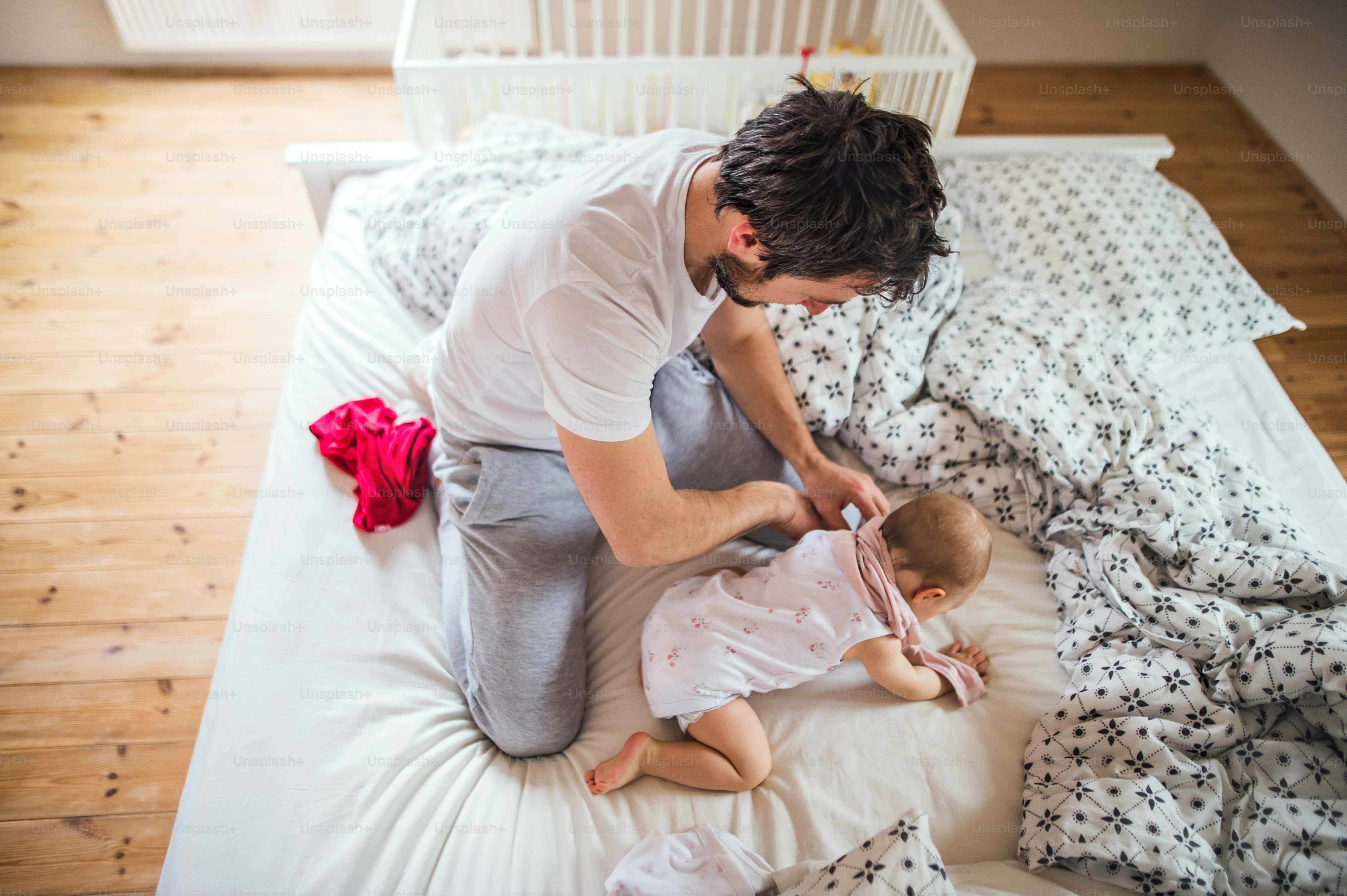 就寝時に自宅でベッドに幼児の女の子を持つ父親。育児休暇。