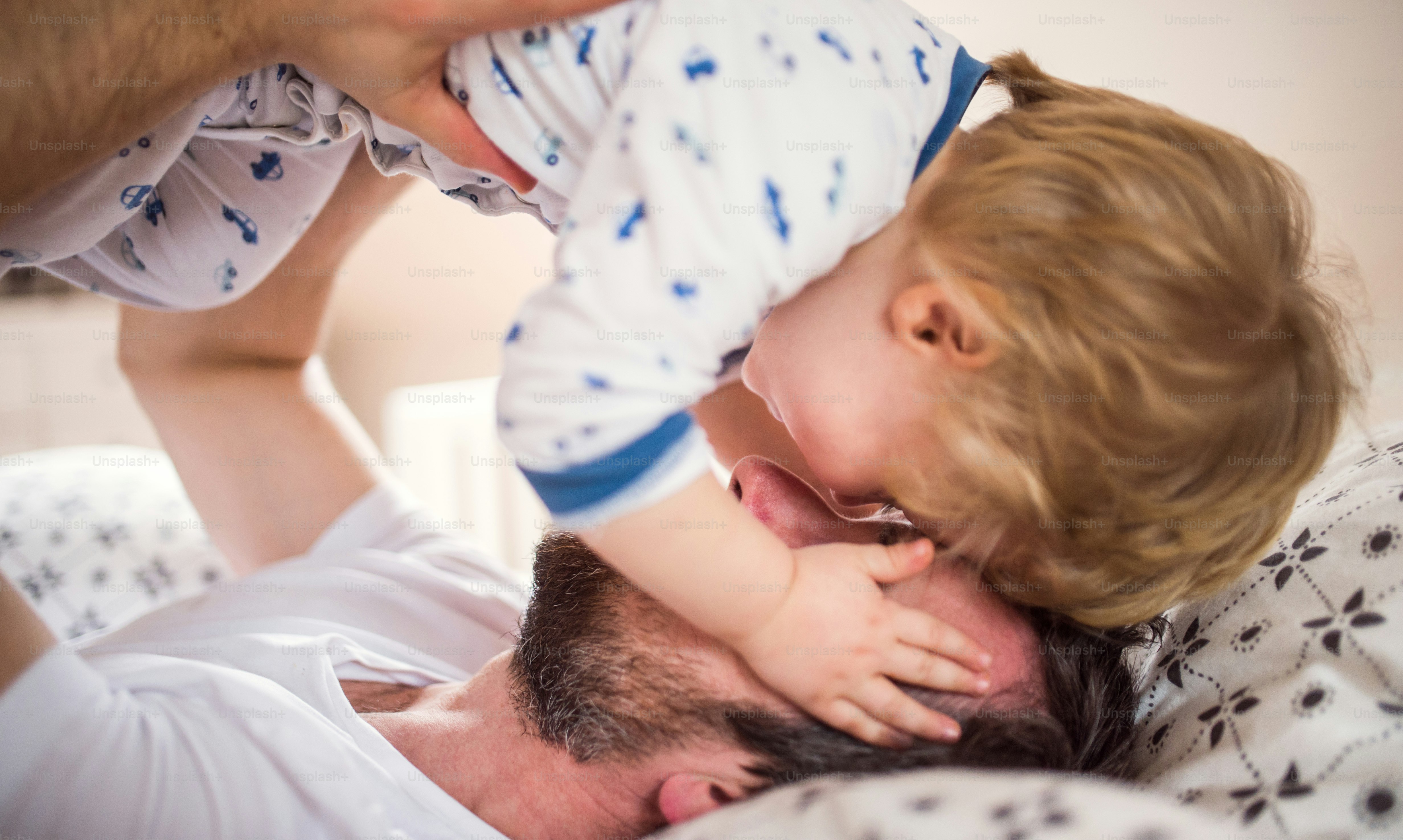就寝時に自宅の寝室で楽しんでいる幼児の男の子を持つ成熟した父親。育児休暇。クローズアップ。