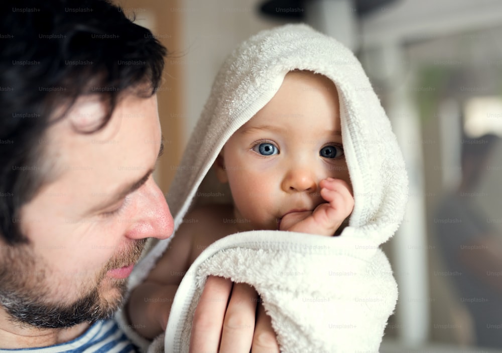 Father with an happy toddler child wrapped in a towel in a bathroom at home. Paternity leave. Close up.
