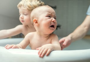 Um pai irreconhecível lavando duas crianças infelizes no banho no banheiro de casa. Uma menina pequena chorando. Paternidade.